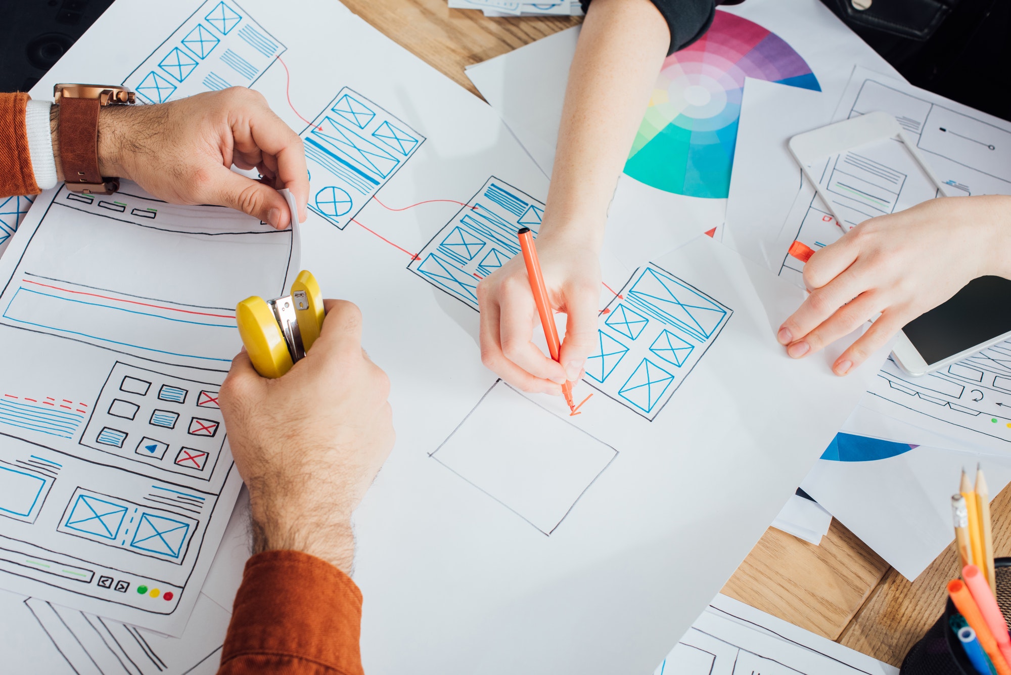 Cropped view of ux designers with stapler and marker planning app frameworks near smartphone on